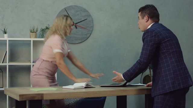 Frustrated male executive caught pretty carefree assistant relaxing with feet up at desk in boss office. Charming office worker resting at supervisor office and holding feet on table caught by manager