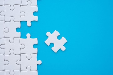Unfinished white jigsaw puzzle on blue background with copy space. Business strategy teamwork and...