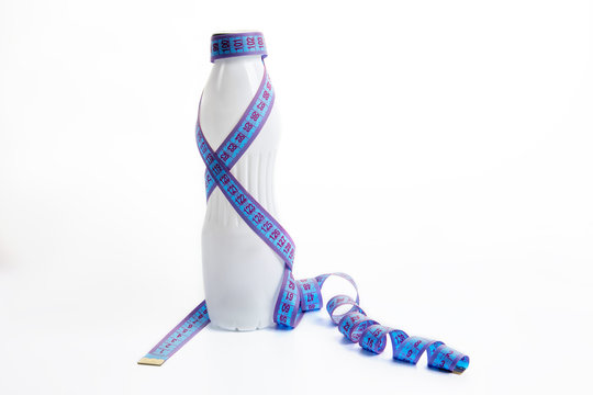 A bottle of yogut wrapped with a measuring tape, on a white background. The concept of weight loss and a healthy lifestyle