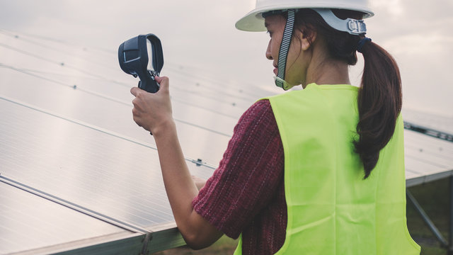 woman engineer checking heat of solar panel and using ir camera to scan heating of panel at solar power plant ; infrared camera using for checking and maintenance power plant of solar