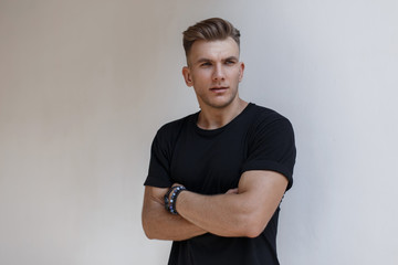 Fashionable handsome american model man with hairstyle in black trendy t-shirt near white wall