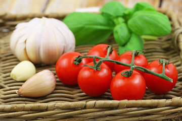 Selection of fresh organic ingredients for pasta: cherry tomatoes, garlic and basil on wicker tray
