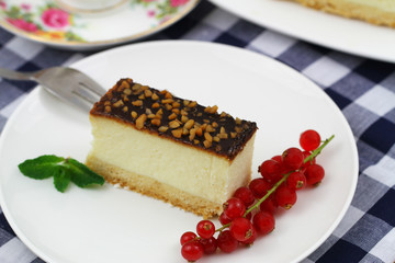 Slice of baked cheesecake with chocolate topping sprinkled with nuts and red current
