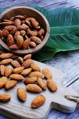 Almond nut on wooden cutting board on wood table with green leaf background, copy space