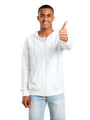 Naklejka premium Dark-skinned young man with white sweatshirt giving a thumbs up gesture and smiling because something good has happened on isolated white background