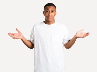 Young african american man having doubts and with confuse face expression while raising hands and shoulders Uncertain concept on isolated background