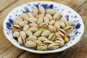 Pistachio nuts on vintage saucer on wooden surface
