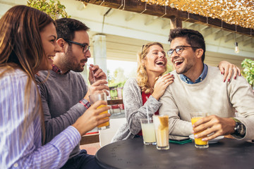 Group of four friends having fun a coffee together. Two women and two men at cafe talking laughing and enjoying their time