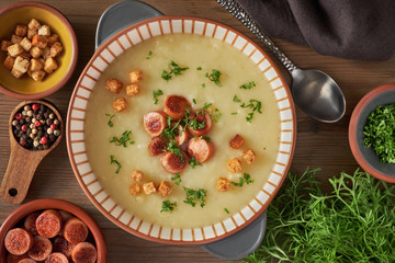 Flat lay of potato cream soup with croutons, fried vienna sausages and green coriander on dark