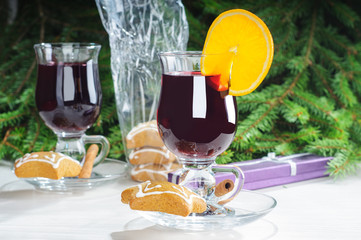 Mulled wine with cinnamon sticks in glass and cookies on the wooden table with christmas tree branch on background