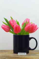 Dank je wel (thank you in Dutch) card with mug full of Dutch pink tulips on wooden surface
