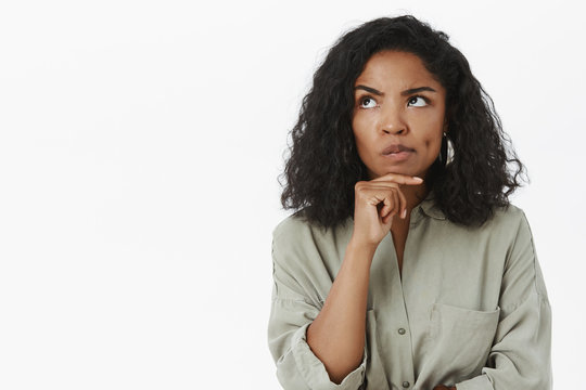 Hmm, maybe it work. Portrait of serious-looking thoughtful and smart businesswoman smirking and frowning looking up with hand on chin while thinking making up plan how make work of office better