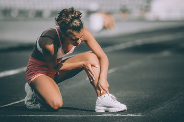woman runner hold her injured leg on track. grey background