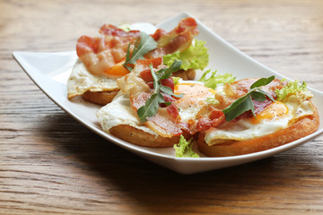 Bruschetta with rucola, chrispy bacon and poached egg served on white plate