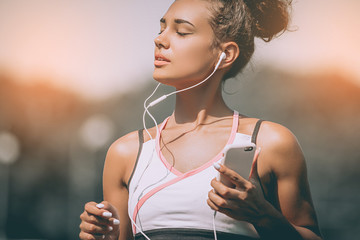 Serious female jogger looking confident. Young fitness woman listening music with headphones after...