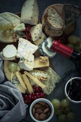 board  with various assortment of french cheese, almonds, nuts, grapes and red wine. Top view on a dark background.Antipasto board.