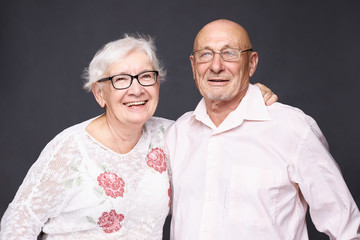 Authentic indoor portrait of glad grey haired wrinkled woman being pleased to meet her first love, leans at senior man`s shoulder, remember pleasant moments of their relationship. Human aging concept.