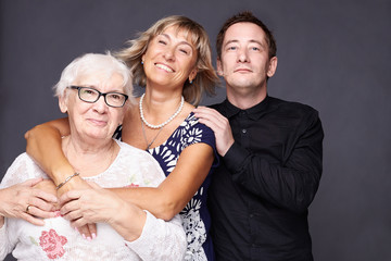 Multi generation concept. Family portrait of mature wrinkled woman dressed in stylish shirt, surrounded with love of  daughter and son who came to congratulate pretty elderly lady with anniversary.