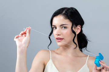 Young woman with dental floss on a gray background