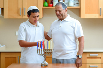 Jewish Boy and dad with deeper skin tones recited blessings on Chanukah menorah and Sing the...