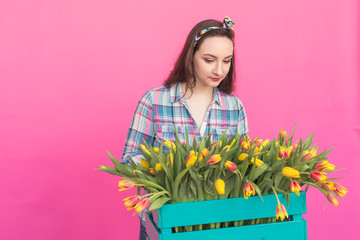 Happy caucasian young woman with box of yellow tulips on pink background