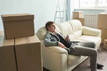 Moving process,real estate and new home concept - tired guy sits on the sofa in the empty room