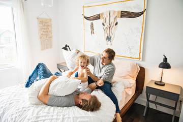 Family with child having fun on bed with pillow fight