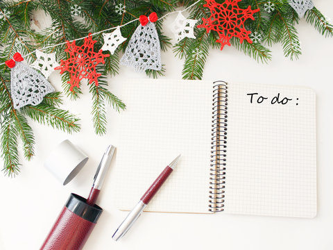 Desktop decorated for new year. Notebook to record a list of Christmas shopping, to do list. Fir branches and garland crocheted, snowflakes and Christmas trees.