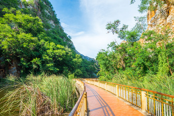 Beautiful rock mountain or hill landscape with clear lake and long walkway in sunny day blue sky. Asia travel destination concept, Ratchaburi Thailand. Traveling on holiday vacation summer season.