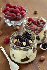 Dessert with chocolate biscuit, cream, hazelnut and fresh berries in glass jars, trifle, vertical