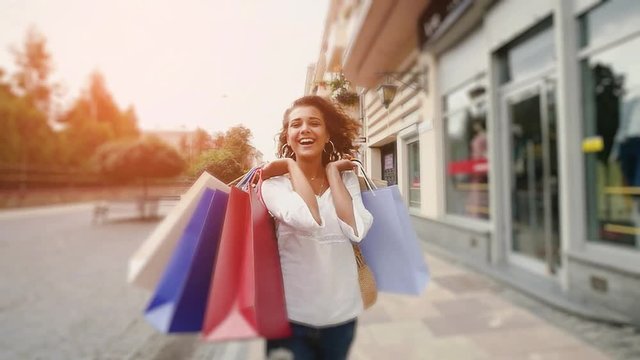 Beautiful smiling woman walking on the street. slow-motion. A beautiful woman walks through the city with shopping bags