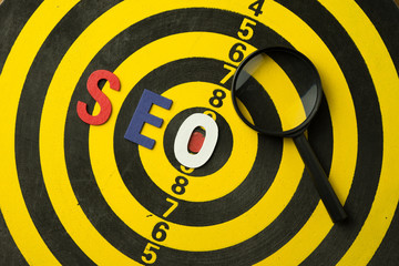 SEO Search Engine Optimization multi color logo alphabets ranking concept on dartboard background with magnifying glass, SEO is one of online marketing business strategy to promote website.