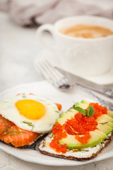 Avocado and red caviar, smoked salmon and fried egg rye toasts for breakfast, close up