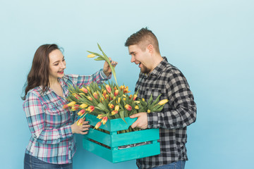 Happy florists fixing tulips in a big wooden box on blue background