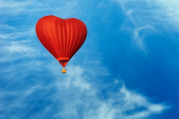 Fototapeta na wymiar Bright red hot air balloon in the shape of heart against blue sky