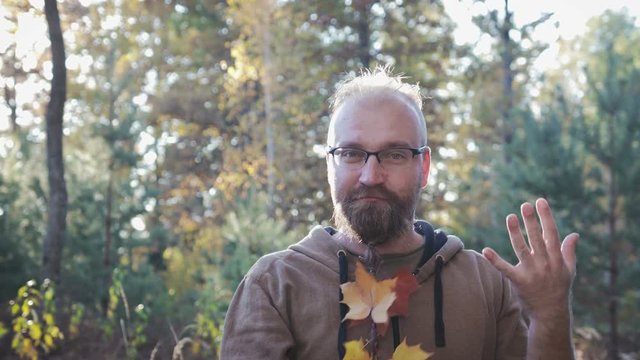 City hipster with glasses and braided leaves in his beard, shows his braid on his chin. It stands against the autumn forest. 4K