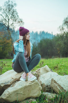 Portrait of young hipster girl enjoying an amazing view of mountains, pretty female traveler, sitting on large stones