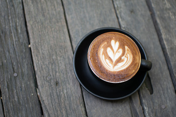 A cup of black coffee is placed on a brown wooden floor.