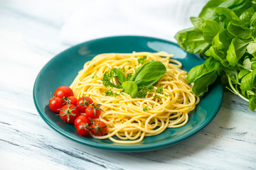 pasta with herbs, basil and tomato served on a green plate in a rustic kitchen
