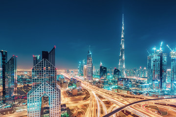 Fototapeta premium Malownicza nocna panorama dużego, nowoczesnego miasta z oświetlonymi wieżowcami. Widok z lotu ptaka centrum Dubaju, ZEA. Wielobarwny tło podróży.