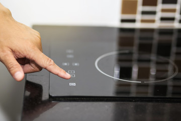 Hand switch on a modern black induction hob in a kitchen. 