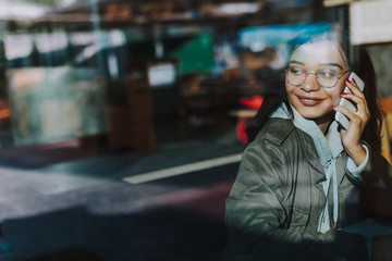 Pleasant phone talk. Young pretty lady turning her head and smiling while sitting alone and having pleasant phone conversation