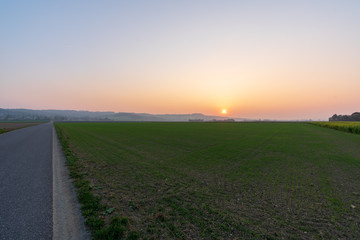 Obraz premium Sonnenuntergang mit Acker und Landstraße