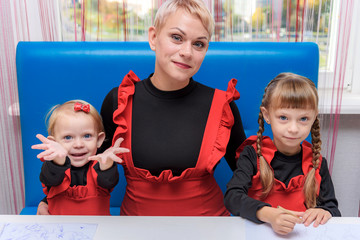 Photo portrait of mother and two cute girls draw on the table in the room.