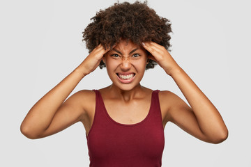 Miserable dark skinned woman feels discomfort, suffers from headache, can not focus, clenches teeth...