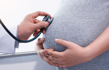 Closeup shot of a doctor using a stethoscope while examining a pregnant woman