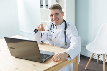 Medicine, working and people concept - doctor sitting at the table with laptop and smiling