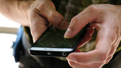 Man tourist with uncleaned hands is looking at an electronic route map in a smartphone, using a navigator in the phone and GPS in a hike and close-up travel