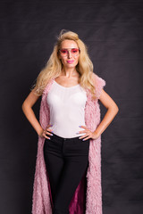 Fashion and beauty concept - blond model with pink glasses dressed in white shirt and pink cardigan over dark background