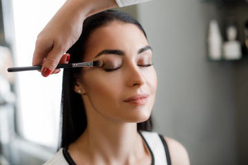 Makeup artist using eyeshadows of dark shades and applying them to corner of woman eye